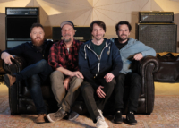 Hanno Busch – Pressefoto (Foto: Claus Fischer Recordings) Vier Musiker sitzen nebeneinander auf einem Sofa in einem Innenraum und schauen in die Kamera.