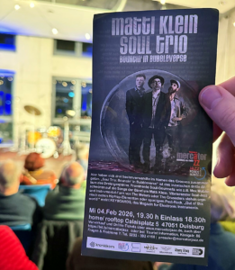 Flyer für das Konzert „Matti Klein Soul Trio – Bouncin’ in Bubbleverse“ im Mercator Jazz in Duisburg, gehalten vor einer Bühne mit Schlagzeug im Hintergrund