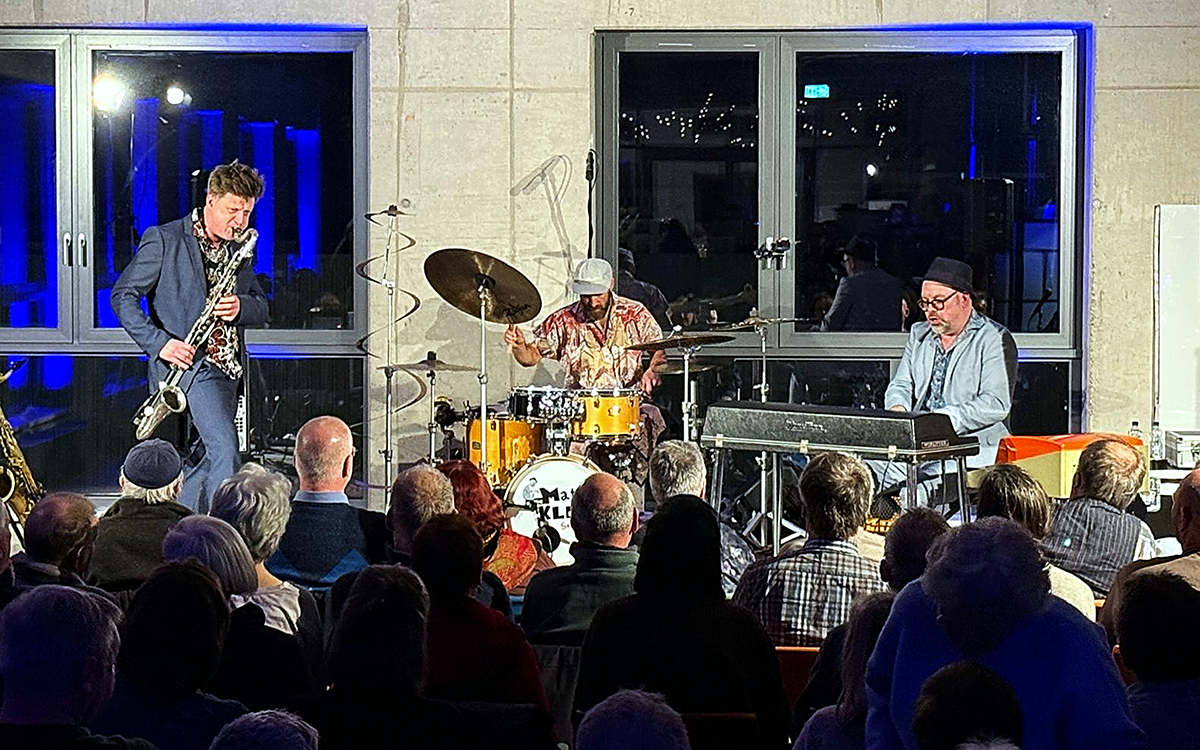 Matti Klein Soul Trio live auf der Bühne bei einem Konzert, mit Publikum im Vordergrund und Schlagzeug, Keyboard und Gitarre auf der Bühne.